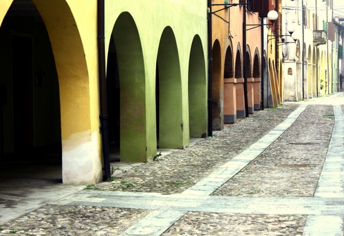 Immagine con strada, lampioni, archi, portici, verde, via, portico, giallo, finestre, colonne, case, porticato, arancione, selciato, balcone