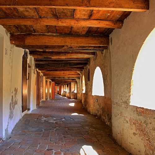 Immagine con legno, archi, portico, travi, porte, porticato, prospettiva, portici, soffitto, mattonelle, finestre, ombre, selciato, luce