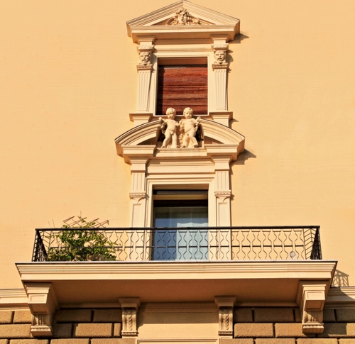 Immagine con balcone, finestra, ringhiera, putti, giallo, pianta, porta, statue, palazzo, statua, finestre, muro