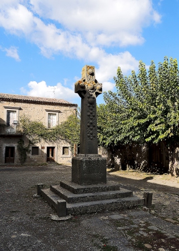 Immagine con alberi, croce, monumento, nuvole, finestre, cielo, gradini, casa, porte, verde, azzurro, scalini, piazzetta, ombra, piedistallo