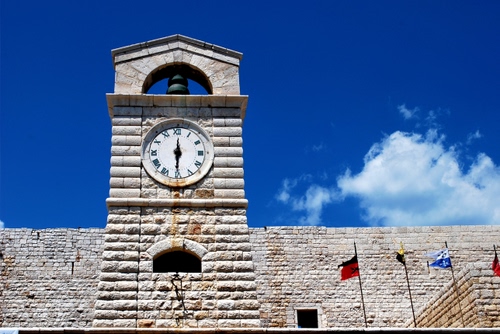 Immagine con bandiere, orologio, campanile, cielo, nuvole, campana, torre, muro