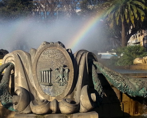 Immagine con arcobaleno, fontana, stemma, acqua, spruzzi, aquila, ovale, palma, colori, palme, verde, marmo, ali, foglie, colonne, rami, alberi