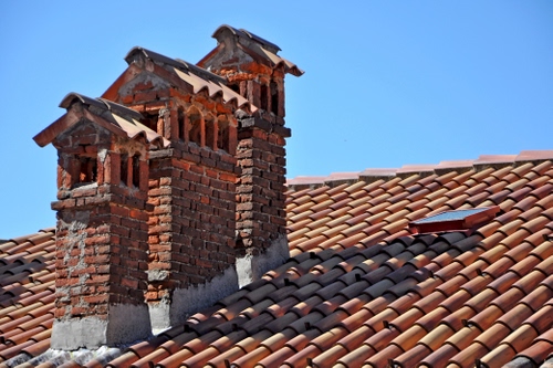 Immagine con tetto, cielo, comignoli, tre, tegole, mattoni, azzurro, coppi, rosso, abbaino, camini, ombre