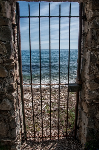 Immagine con mare, cancello, acqua, cielo, spiaggia, ferro, onde, nuvole, porta, serratura, muro, pietre