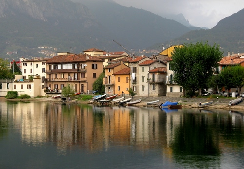 Immagine con barche, acqua, riflessi, case, lago, montagne, finestre, alberi, paese, piante, verde, riva, porte, riflesso, nuvole, borgo, montagna, balconi