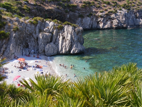 Immagine con mare, spiaggia, rocce, acqua, persone, bagnanti, scogli, piante, palme, scogliera