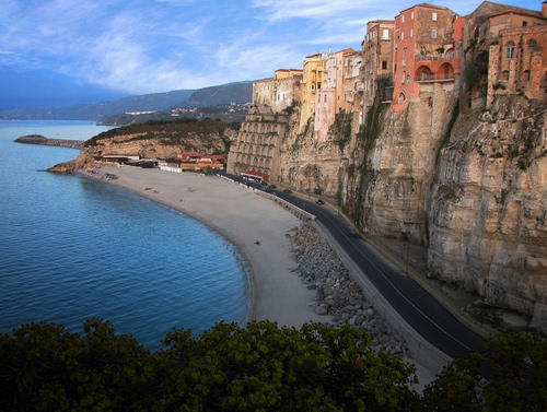 Immagine con strada, case, mare, spiaggia, alberi, scogliera, cielo, costa, sabbia, nuvole, finestre, rocce, acqua, azzurro, roccia, promontorio, borgo, paesaggio, striscia