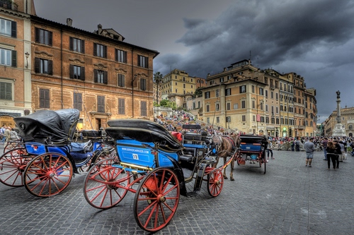 Immagine con ruote, nuvole, piazza, palazzi, rosso, carrozze, cielo, maltempo, case, carrozzelle, azzurro, blu, finestre, persone, gente, cavalli, cavallo