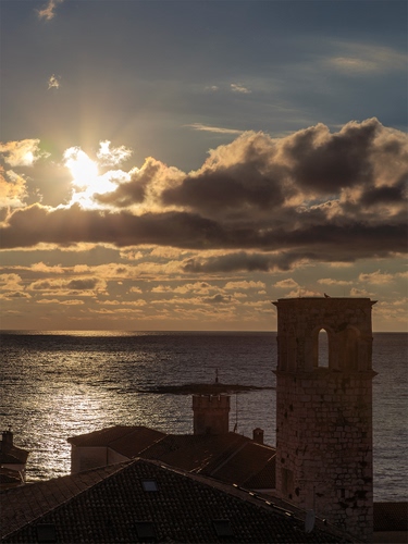 Immagine con nuvole, mare, cielo, controluce, torre, tramonto, tetti, riflesso, sole, campanile, acqua, case, orizzonte, azzurro, luce