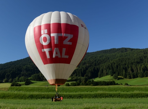 Immagine con mongolfiera, cielo, alberi, prato, rosso, verde, pallone, colline, montagne, bosco, bianco